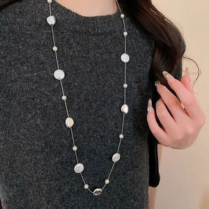 Detail of silver chain long necklace with white pearls on a dark grey sweater
