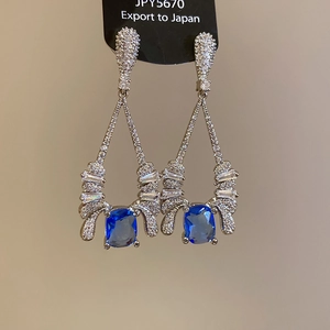 Close-up of teardrop earrings with blue zircon stones and silver needle on black card