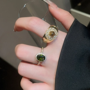 Detail of 18k gold plated tiger eye and green stone rings worn by model holding glass