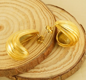 Macro detail of gold-plated ribbed C-shape earrings showing the textured metal surface