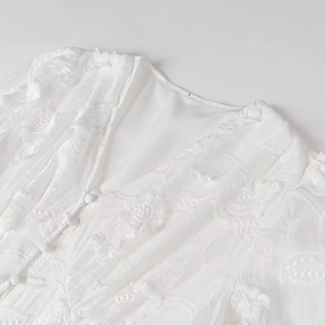 Gros plan des broderies florales sur l'encolure en V de la robe blanche chic