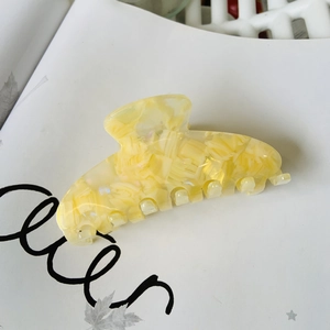 Close-up of a cream yellow marbled acetate hair claw clip on a stylish paper background