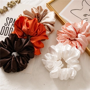 Detailed view of five oversized satin scrunchies in silk-like brown and gold earth tones