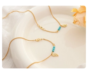 Detail of gold titanium steel anklet with turquoise beads and wing pendants on linen