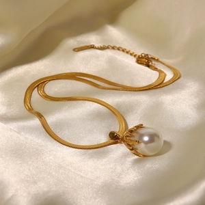 Close-up of golden snake chain necklace with a large baroque pearl on white satin