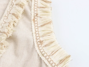 Vue détaillée du tissu en lin beige avec des glands en fil d'or sur une robe à col en V