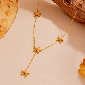 Détail du collier en Y avec pendentifs étoile de mer dorée sur un fond beige chaleureux