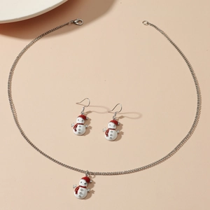 Detail of cute snowman necklace and earrings set with red and white enamel on pink background
