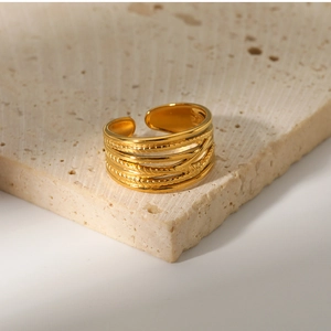 Detail of layered gold titanium steel ring on a minimalist beige travertine stone base