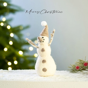 Handmade wool felt snowman ornament on a snowy base with warm Christmas lighting