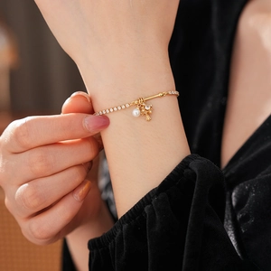 Close-up of golden pearl bracelet with zircon cross charm and tennis chain on wrist