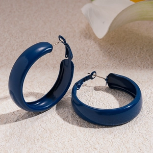 Gros plan de boucles d'oreilles créoles bleu foncé brillantes sur une surface beige texturée