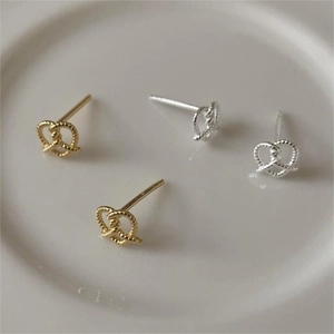 Detailed view of silver and gold knotted twist heart stud earrings on a ceramic dish