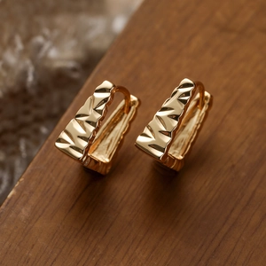 Macro detail of geometric gold-plated hoop earrings with faceted texture on wood