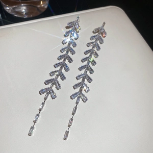 Détail macro de boucles d'oreilles à pompons argentés avec zircons sur cuir blanc