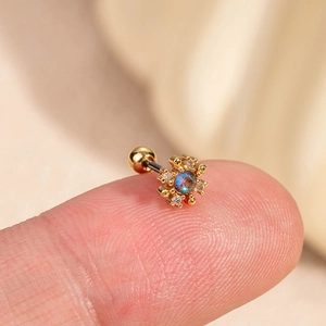 Gros plan détaillé d'une boucle d'oreille fleur en or avec zircon coloré sur un doigt