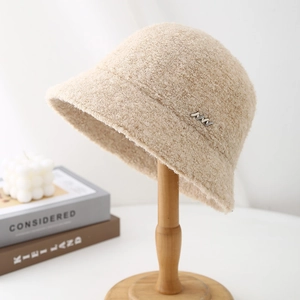 Detail of beige bouclé bucket hat with silver MM metal emblem on wooden stand