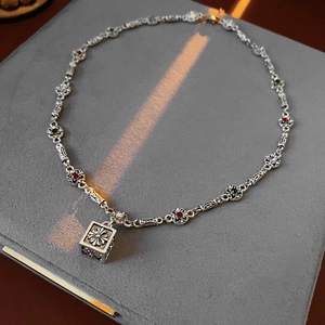 Close-up of vintage silver necklace with red and green gems and cross square pendant