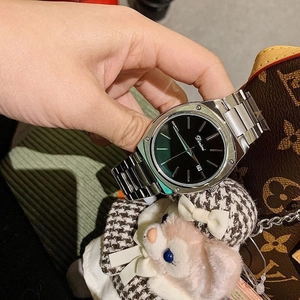 Detail of silver steel watch with green square dial and calendar display held by hand