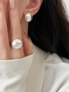 Close-up of silver geometric stud earrings with textured surface and beaded edge detail
