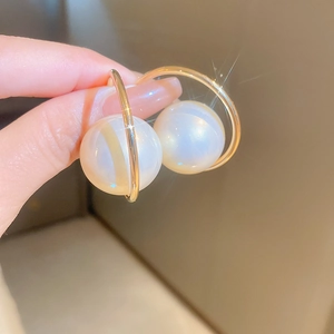 Close-up of gold C-shaped earrings with large white pearls and a brilliant sparkling finish