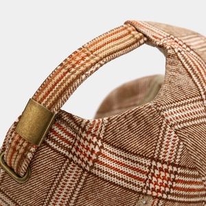 Close-up of houndstooth baseball cap featuring adjustable bronze buckle and metal strap