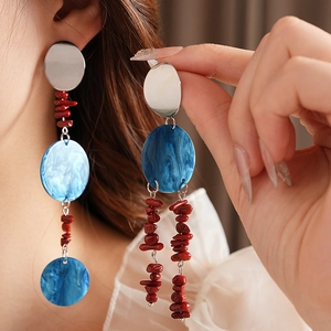 Close-up of asymmetric tassel earrings with red beads and blue charms worn by a model