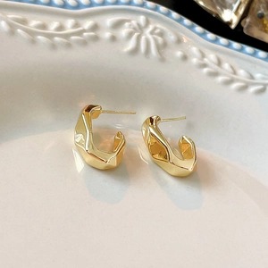 Detail of irregular geometric gold-plated earrings resting on a white ceramic plate