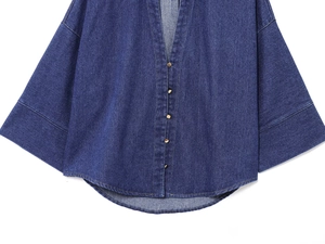 Dettaglio della camicia di jeans blu con bottoni metallici e polsini larghi