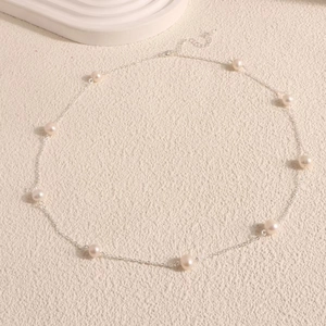 Detailed view of fresh water pearl necklace with silver chain and lobster clasp on beige texture