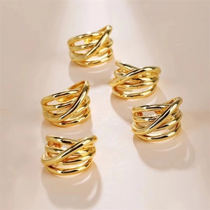 Top view of five golden multi-layer crisscross rings with polished mirror finish on pink background