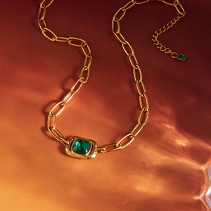 Gold chain necklace with a deep green square gemstone pendant over water ripple shadows