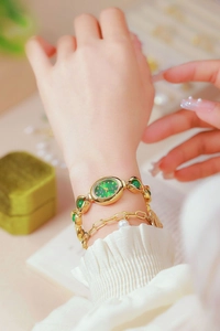 Detail shot of a gold oval watch with green dial and matching gemstone bracelet on wrist