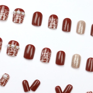 Short round red press-on nails with champagne pearls, glitter, and plaid patterns