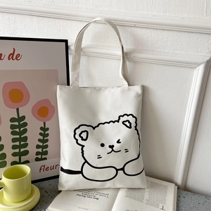 Detail of white canvas tote bag with black line art cartoon bear in a lifestyle setting
