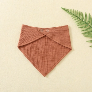 Macro detail of red-brown double gauze baby bib showing cotton texture and metal snap button