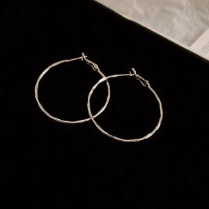 Macro shot of silver C-shaped hoop earrings with hammered metal texture on dark background