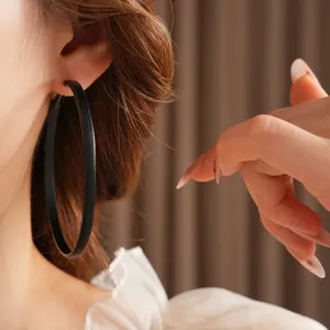 Grandes créoles minimalistes noir mat portées par un mannequin pour un look chic