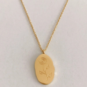 Detail of a golden oval pendant featuring a delicate rose flower engraving on a cable chain