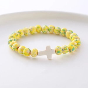Detail of yellow and green spotted stone beads with a white cross charm on a tray