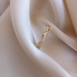 Macro shot of gold twisted braided ring with sparkling zircon inlays on beige silk