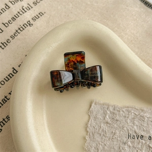 Detailed close-up of a small tortoise shell acetate bow hair claw clip on ceramic tray