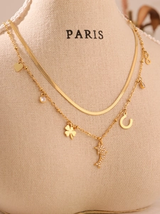 Detail of a double-layered gold necklace with dolphin and clover charms on a beige bust