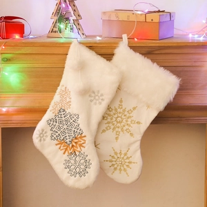 White plush Christmas stockings with snowflake embroidery hanging on a festive fireplace