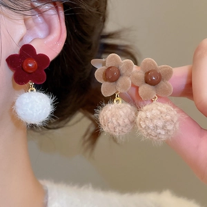 Detailed close-up of velvet flower earrings with fuzzy pom poms in red and khaki