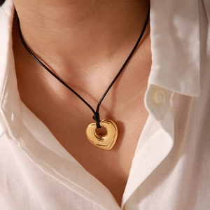 Close-up of a gold hollow heart pendant necklace with a black cord on a model