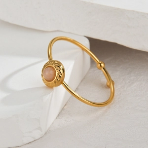 Detail of 14K gold stainless steel ring with pink gemstone on white stone pedestal