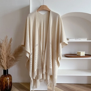 Detailed close-up of beige knit shawl featuring hollowed-out patterns and tassel hem details