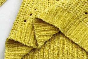 Close-up of mustard yellow chenille sweater showing ribbed cuffs and hollow knit texture
