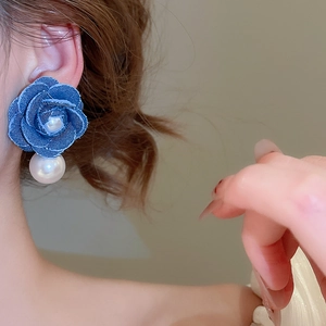 Detail of denim fabric rose earring with large white pearl on model's ear
